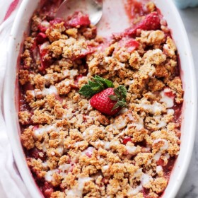 Overhead view of strawberry crumble in an oval baking dish with a spoon resting in the space where a few scoops are missing.