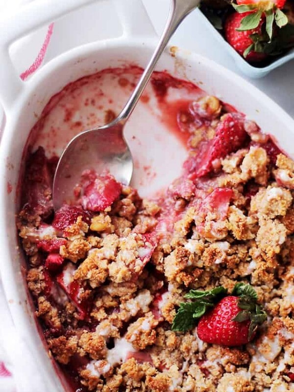 Overhead view of strawberry crumble in an oval baking dish with a spoon resting in the space where a few scoops are missing.