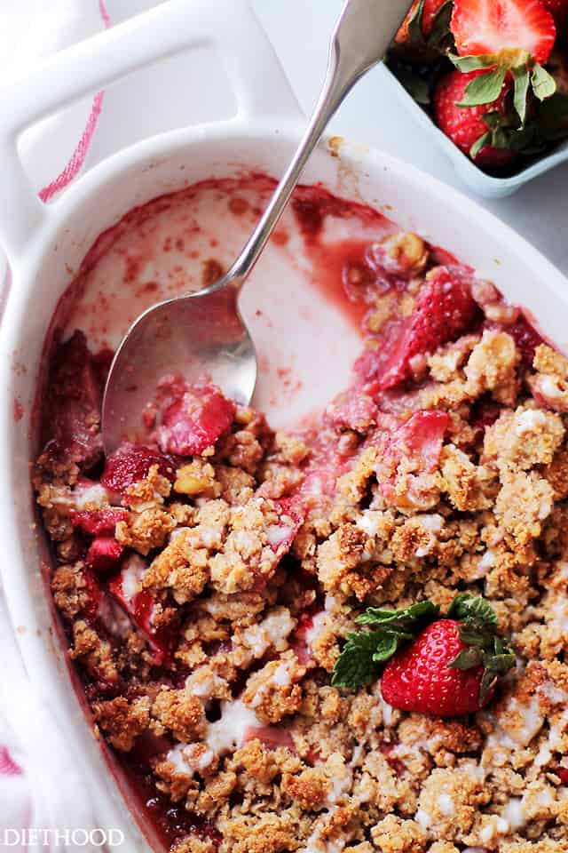 Overhead view of strawberry crumble in an oval baking dish with a spoon resting in the space where a few scoops are missing.