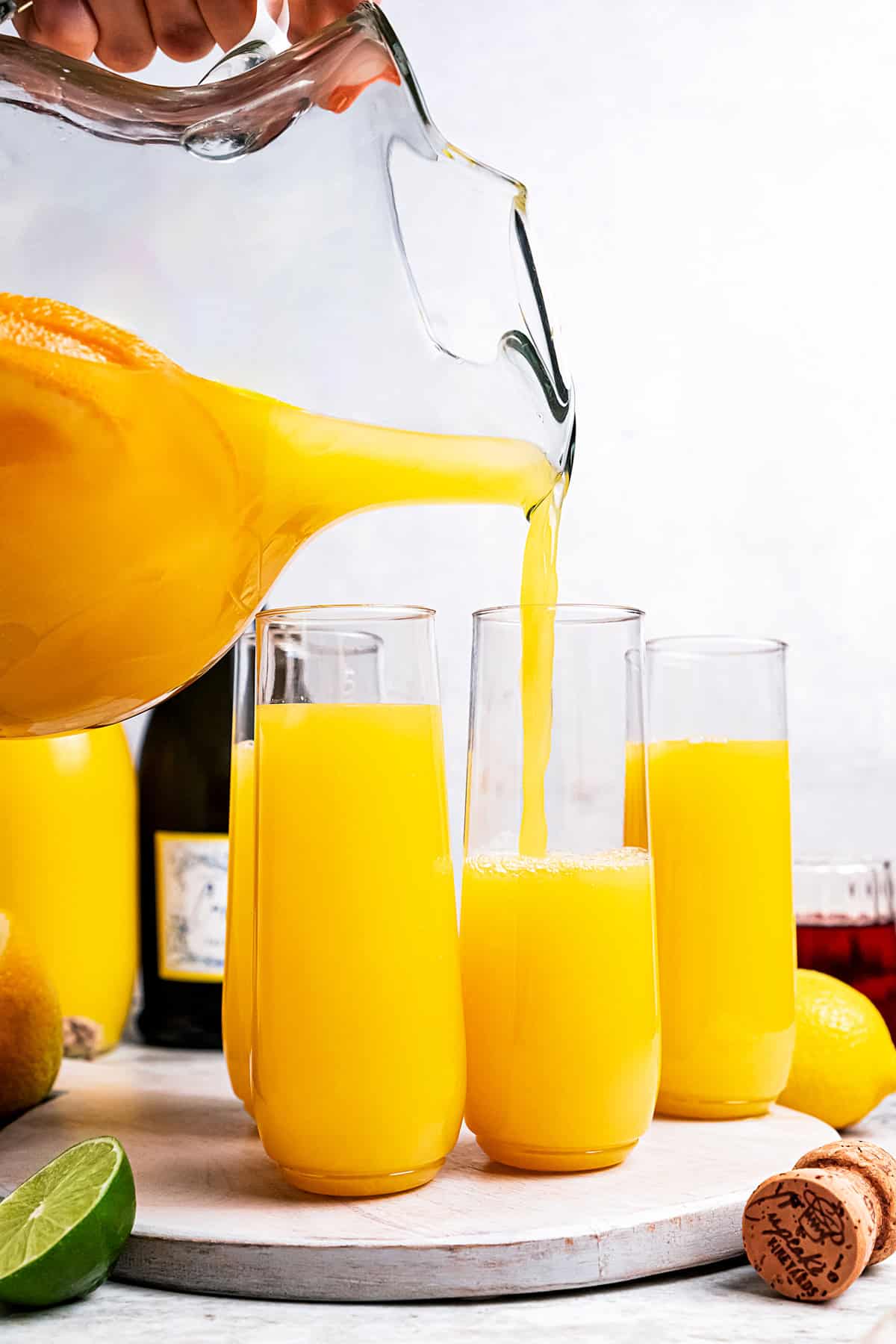 Orange juice being poured from a pitcher into flute glasses on a tray.
