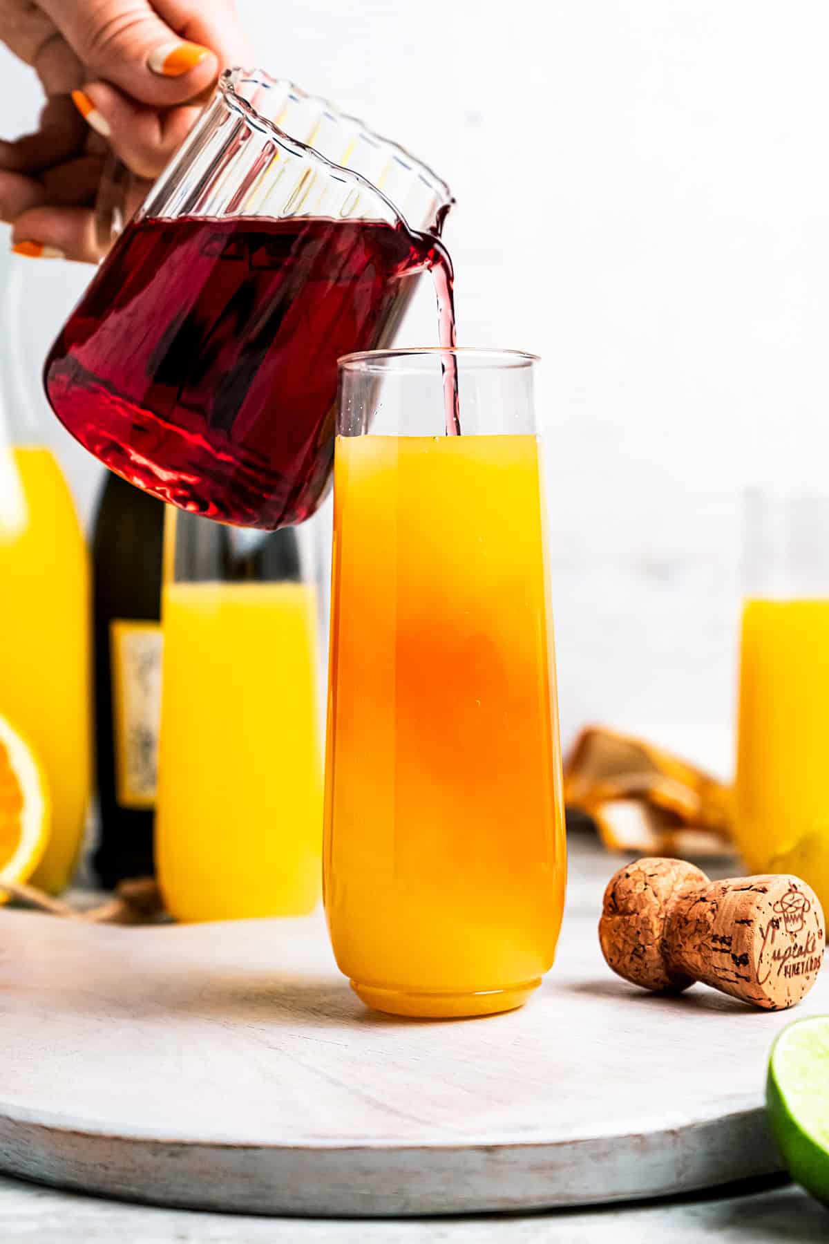 Female hand pouring cranberry juice into a mimosa in a flute glass.