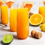 Several stemless flute glasses filled with orange juice and prosecco and arranged on a white surface.