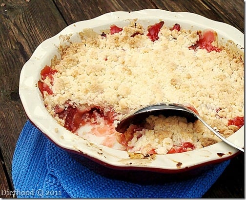 STRAWBERRY RHUBARB CRUMBLE in a pie plate with large metal spoon.