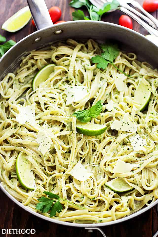 Avocado pasta garnished with shaved parmesan and basil leaves in a skillet.
