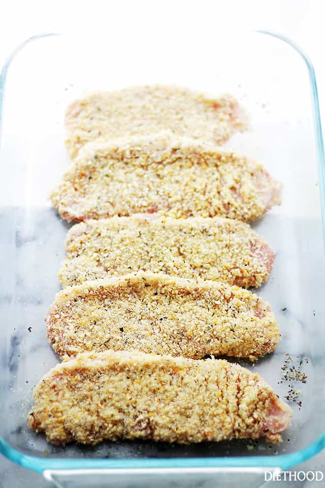 Raw pork chops lined up in a dish with breading coated over them.