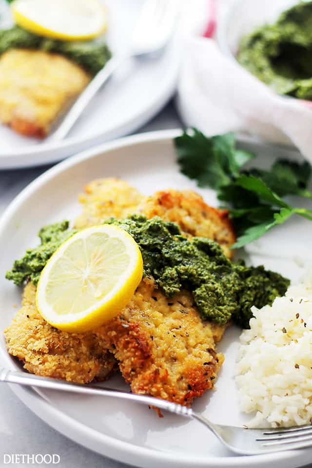 A plate of Easy Breaded Pork Chops with creamy pesto on top, along with a single slice of lemon.