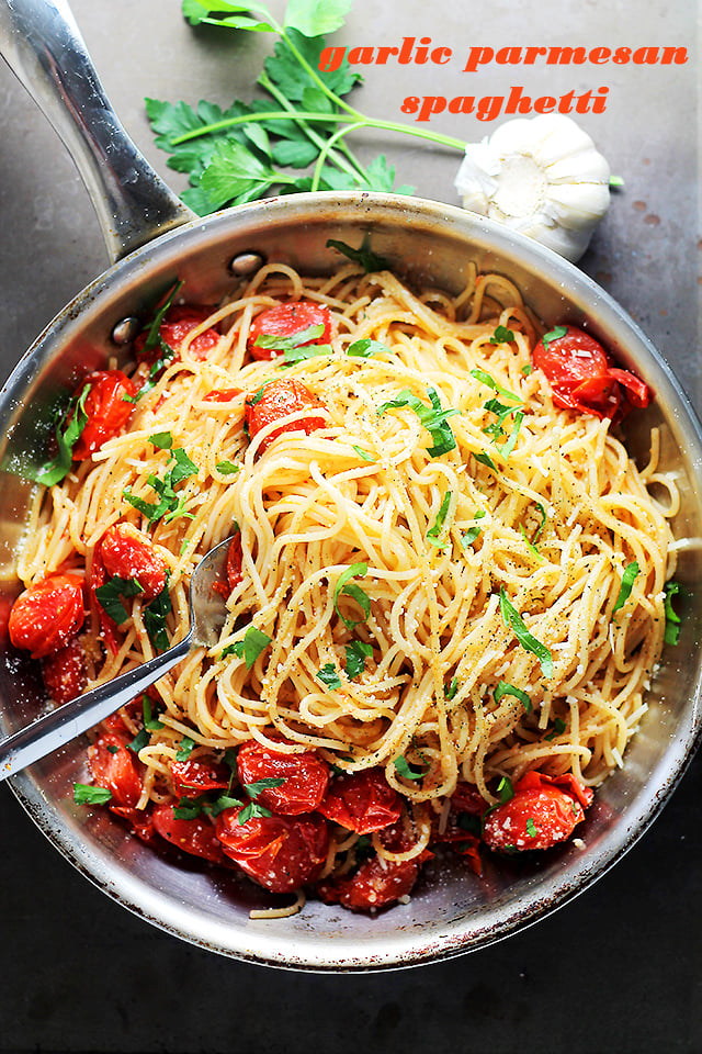Overhead image of a skillet with cooked spaghetti, blistered tomatoes, parmesan cheese, and a garnish of fresh basil.