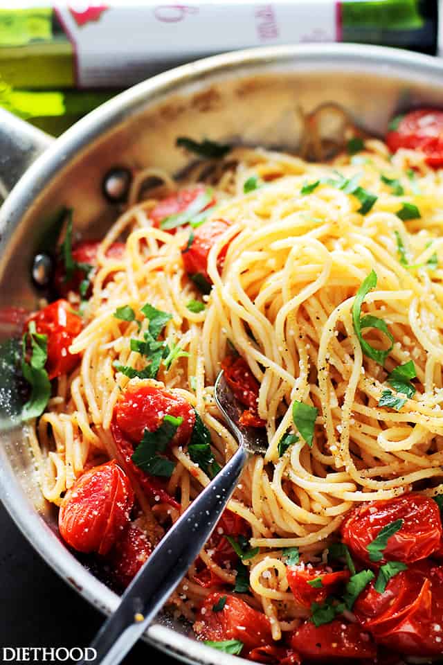 Tossing spaghetti with cherry tomatoes in a skillet.