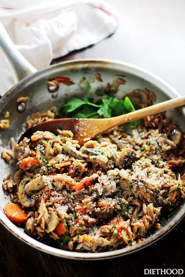 Mushroom orzo pilaf in a metal skillet with a wooden spoon.