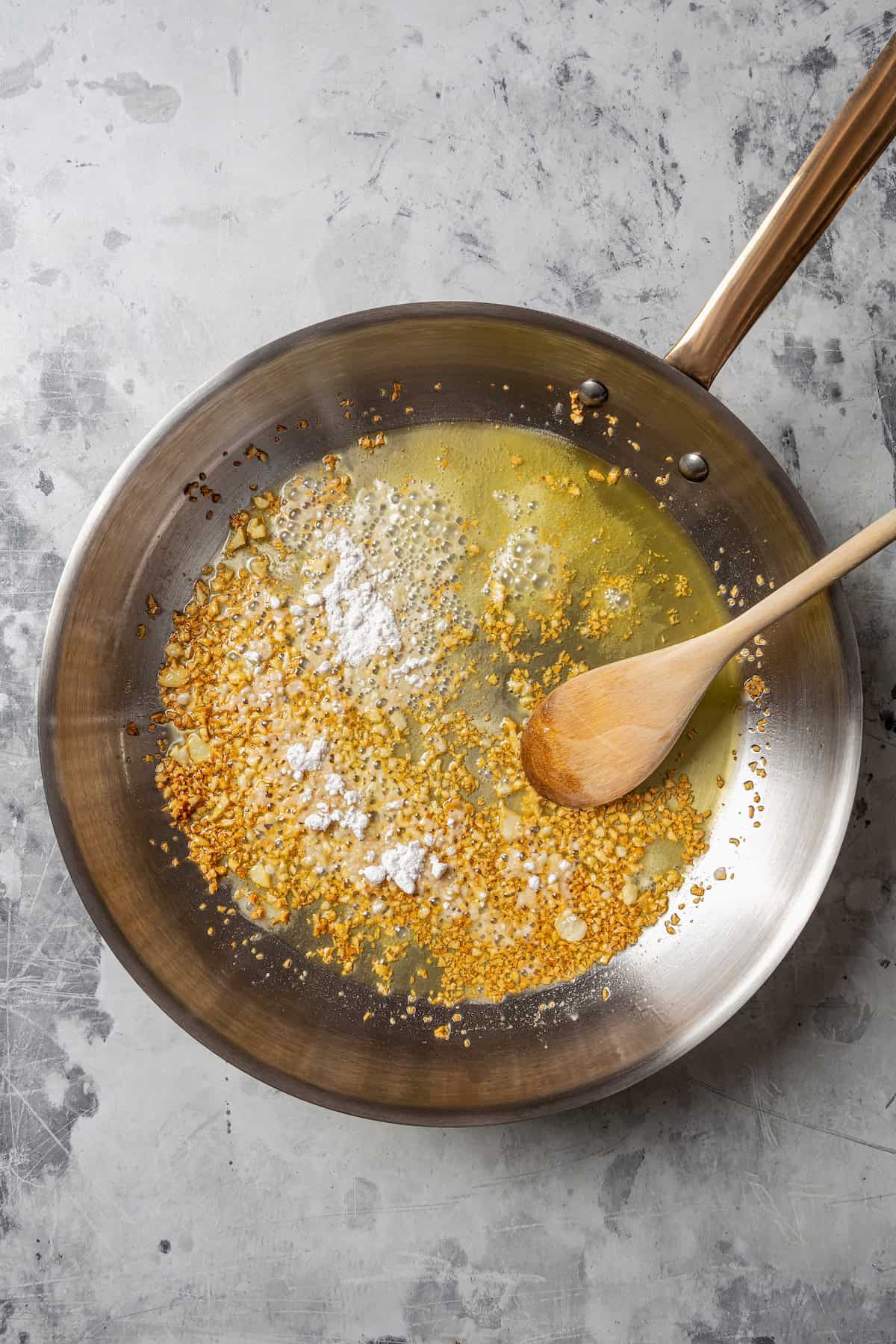 Flour stirred into sautéed garlic in a saucepan to make a roux.