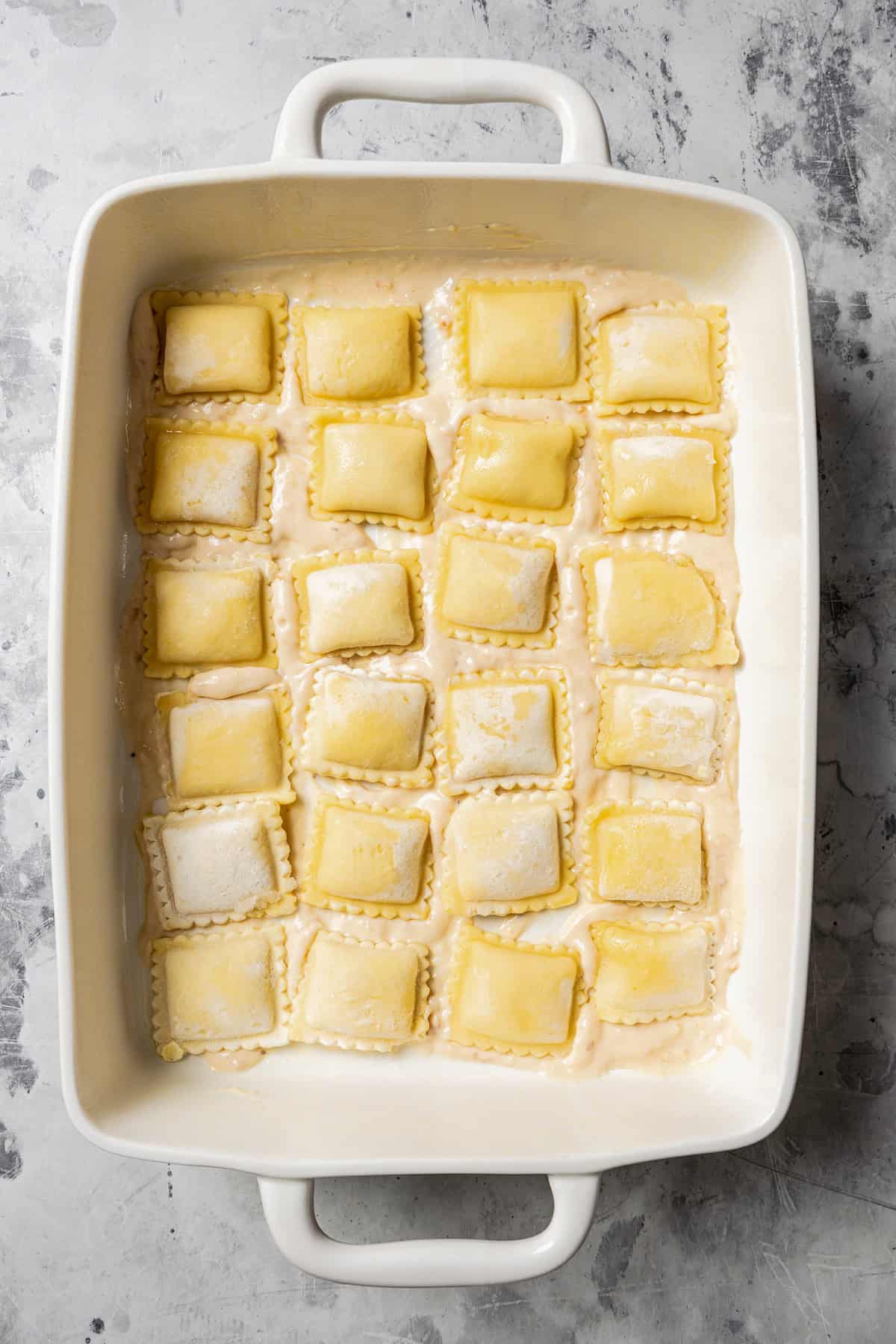 Raviolis arranged in rows in the bottom of a ceramic baking dish.