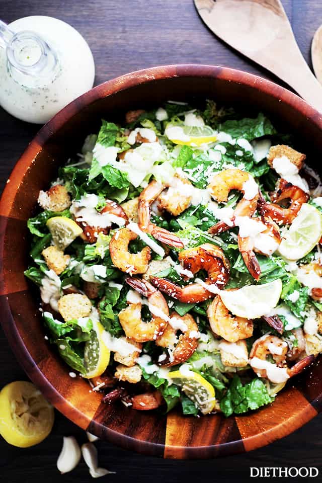 Caesar salad in a serving dish, topped with grilled shrimp and creamy dressing.