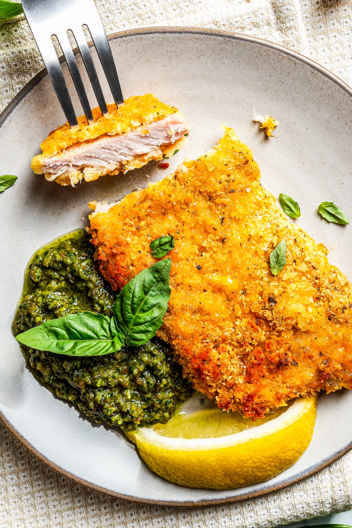 Taking a bite out of breaded pork chops served on a plate with bacon-kale pesto and a slice of lemon.