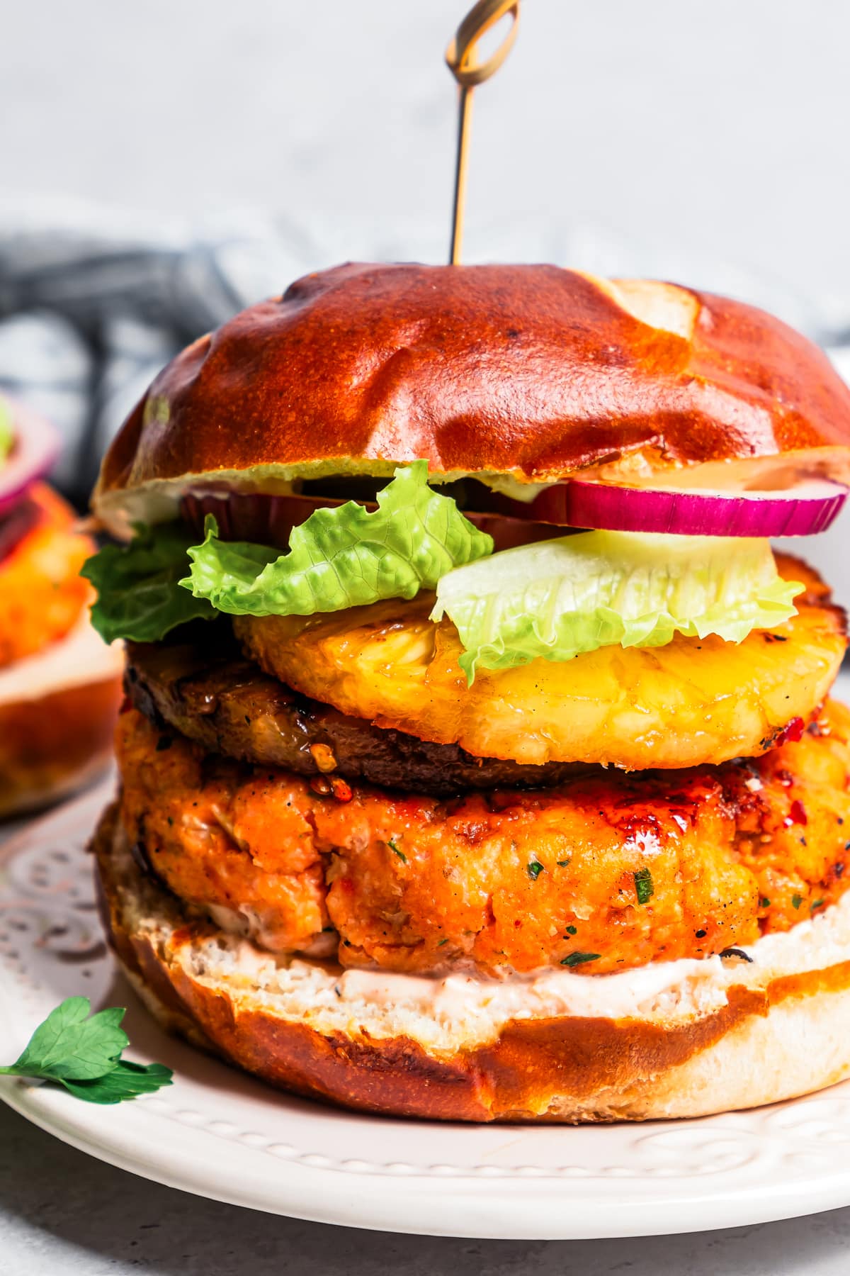 Close up shot of a tall salmon burger piled up with pineapple rings, salad greens, and red onions.