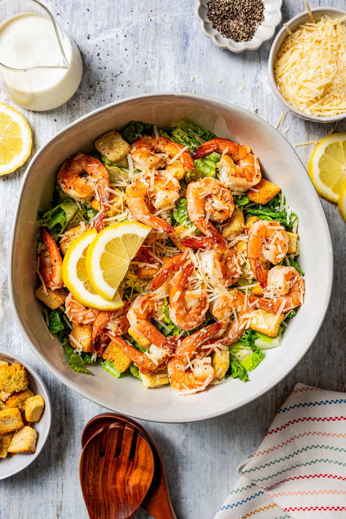 Shrimp Caesar salad in a large bowl garnished with lemon wedges, surrounded by salad ingredients.