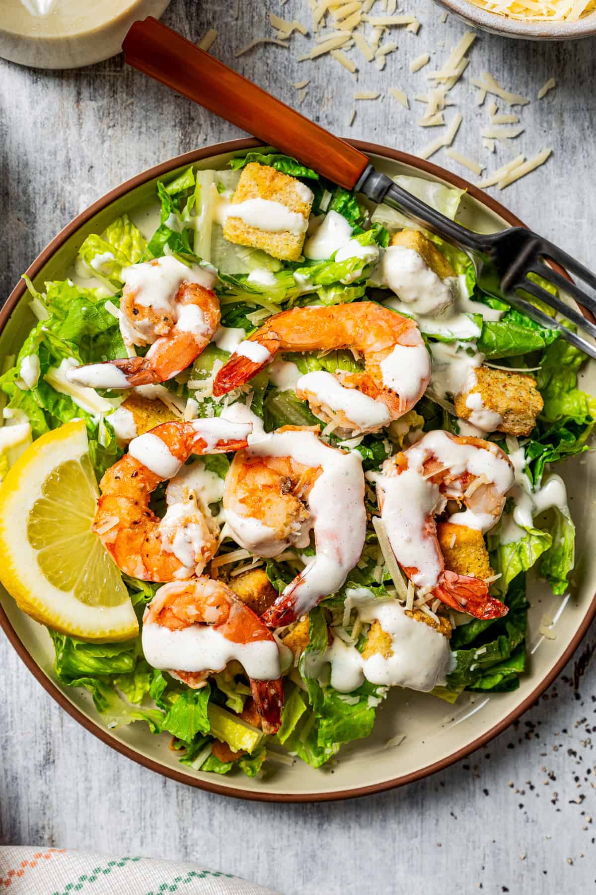 Caesar salad topped with grilled shrimp and a drizzle of dressing, garnished with a lemon wedge on a plate.