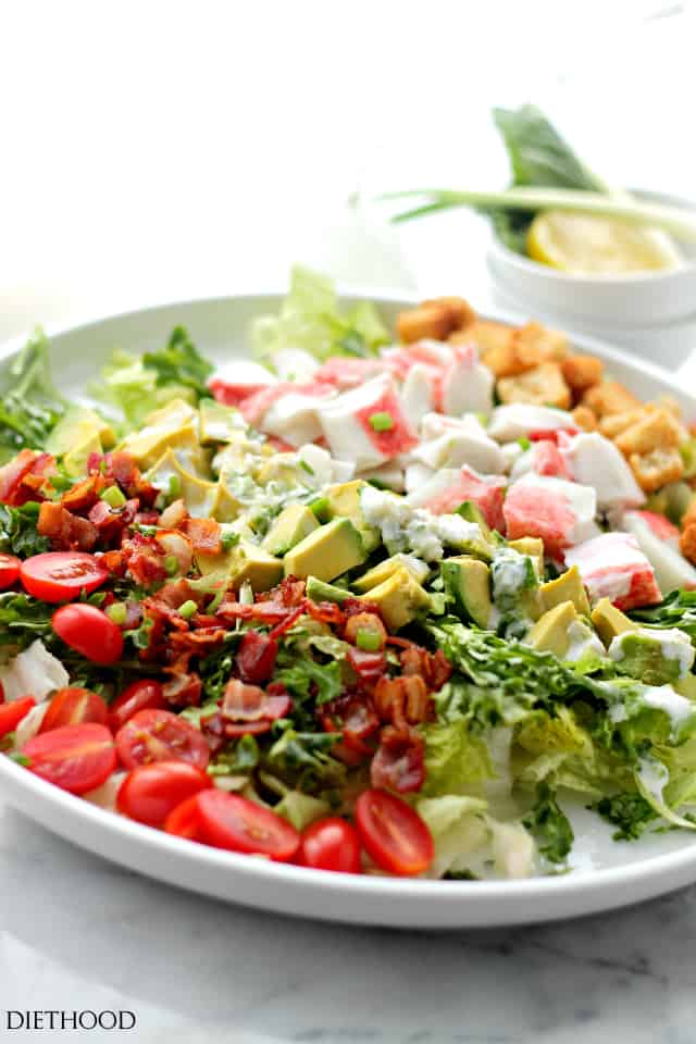 Avocado crab salad with bacon, tomatoes, and croutons topped with creamy dressing in a large bowl.