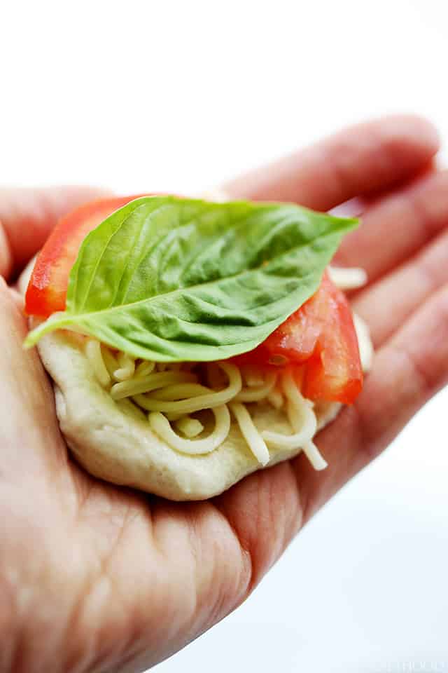 A hand holding a round of biscuit dough with mozzarella, tomato, and basil.