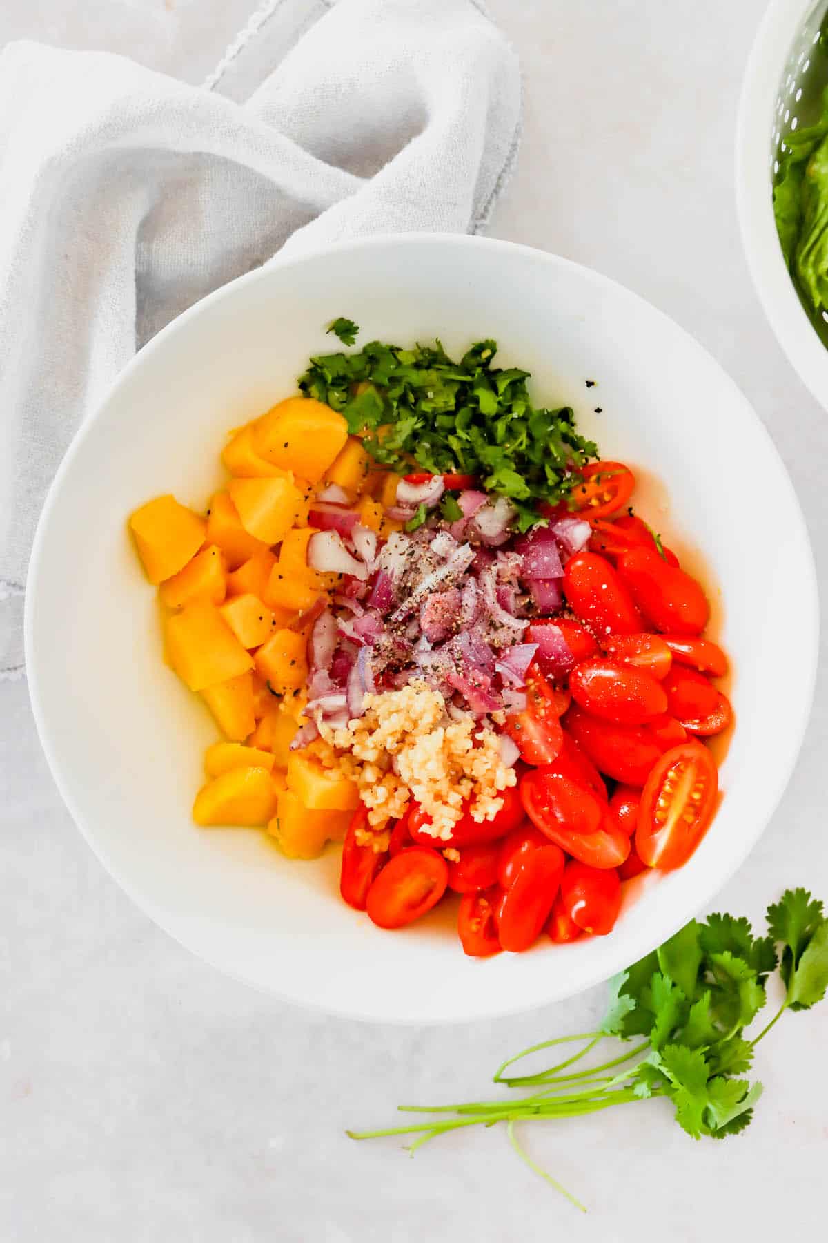 Mango, garlic, cilantro, and cherry tomatoes in a white bowl