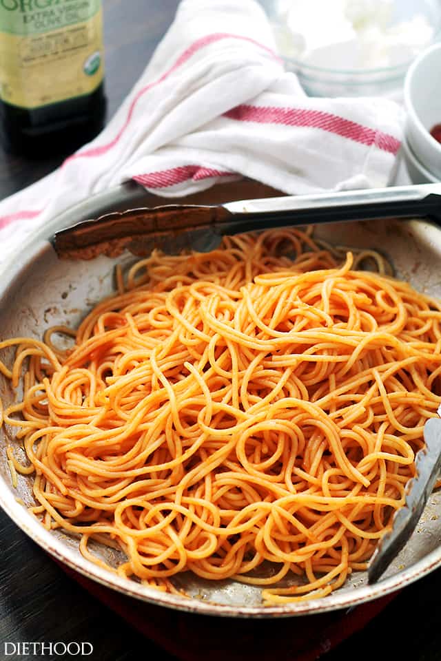 A skillet with spaghetti tossed in red sauce.