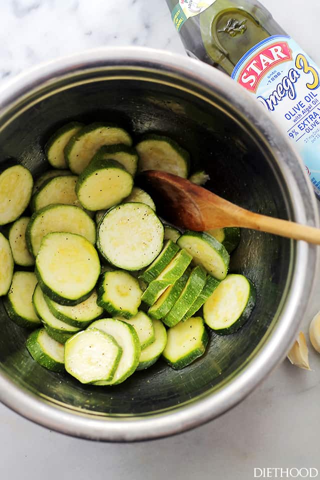 Zucchini slices in a mixing bowl with a wooden spoon stirring through them.