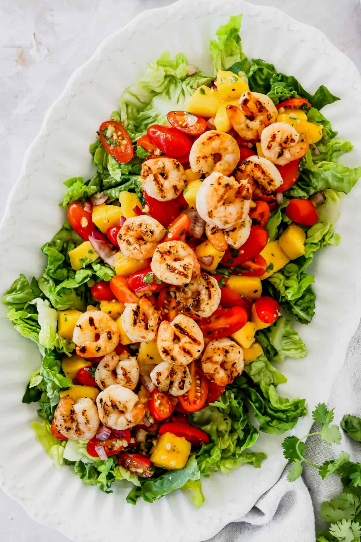serving platter with shrimp, mangoes, and cherry tomatoes arranged over salad greens.