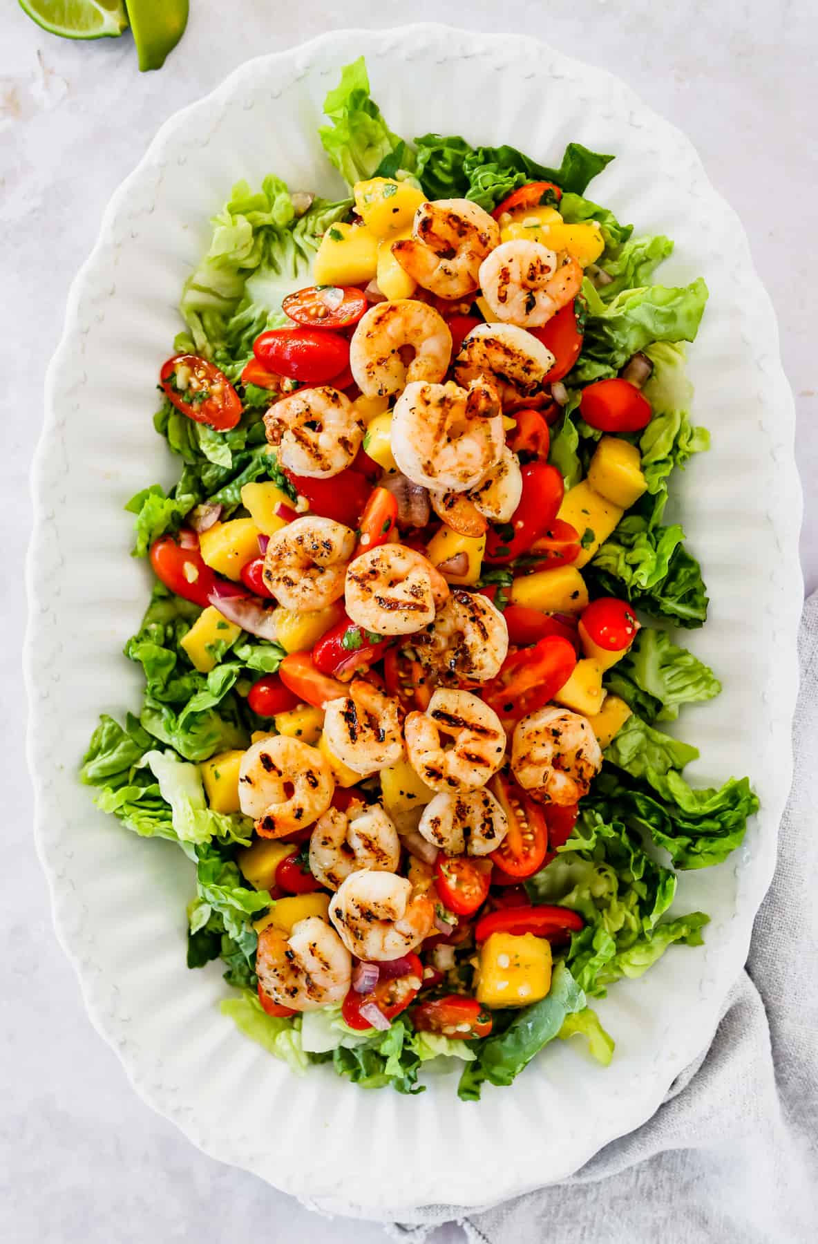 Oval serving platter with shrimp, mangoes, and cherry tomatoes arranged over salad greens.
