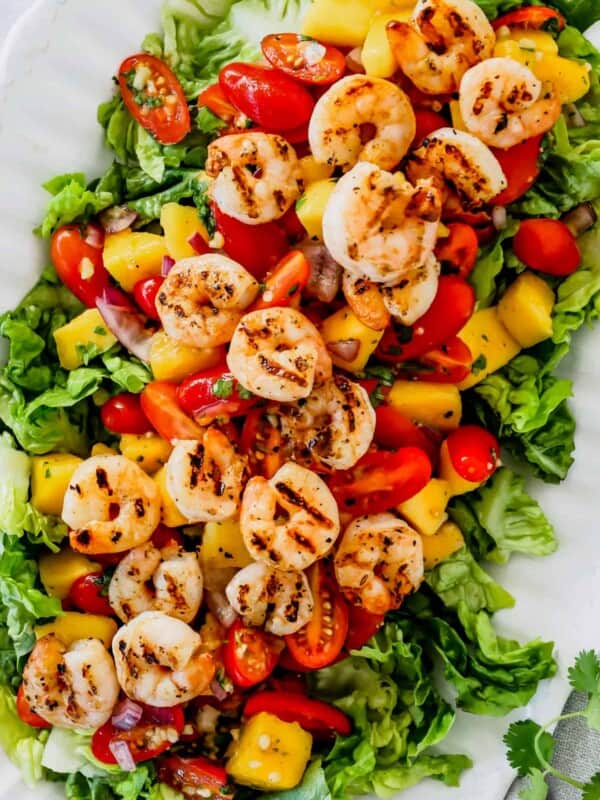 Close-up of a serving platter with shrimp, mangoes, and cherry tomatoes arranged over salad greens.