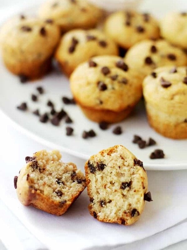 Close up of a mini chocolate chip muffin cut in half in front of a plate full of more chocolate chip muffins.