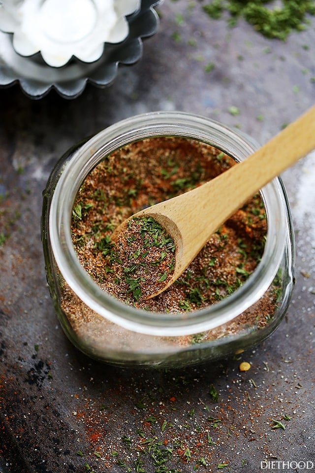 Homemade Jamaican Jerk Seasoning in a small jar, with a wooden spoon stirring through it.