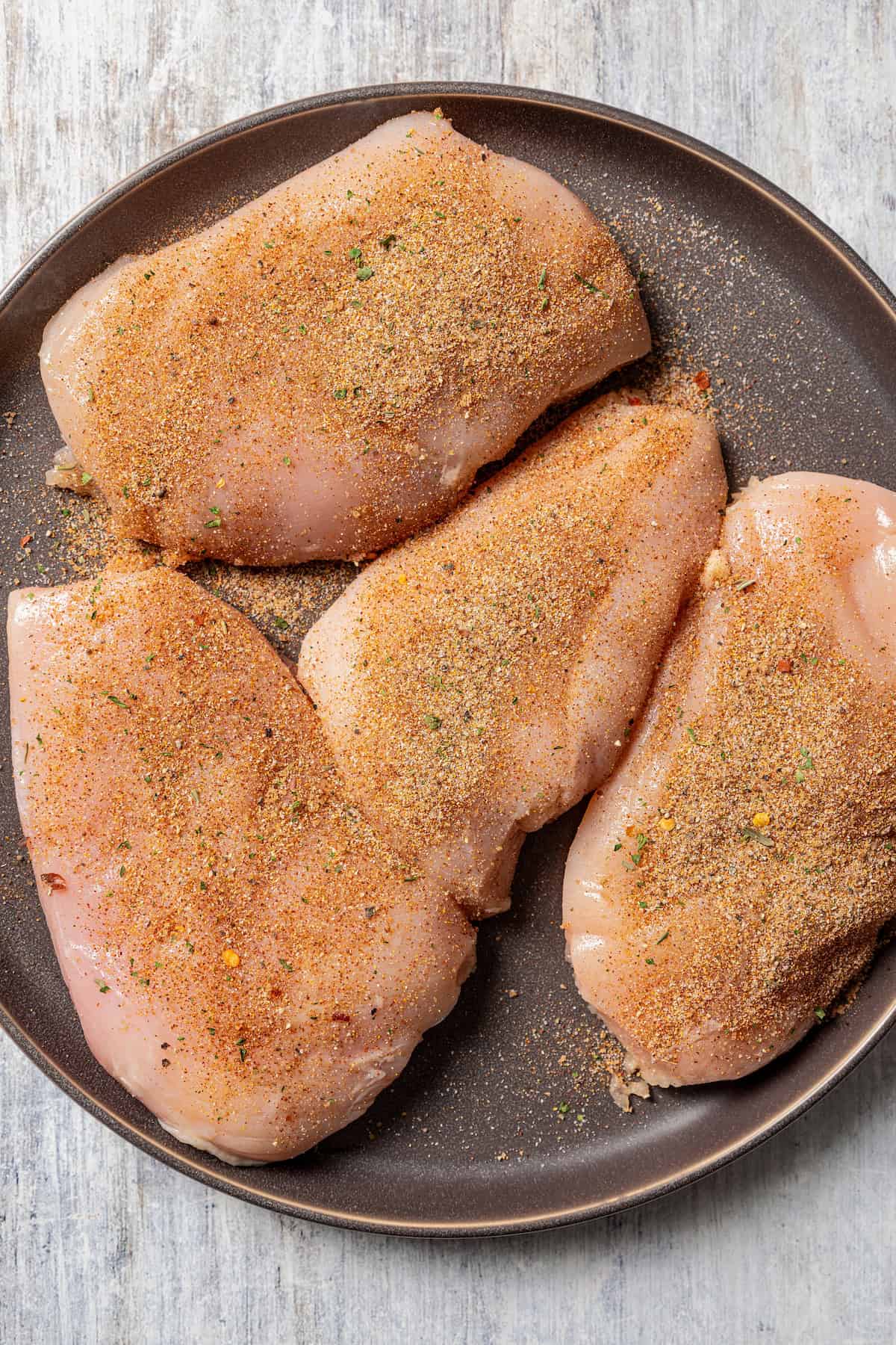 Four seasoned chicken breasts on a grey stoneware plate.