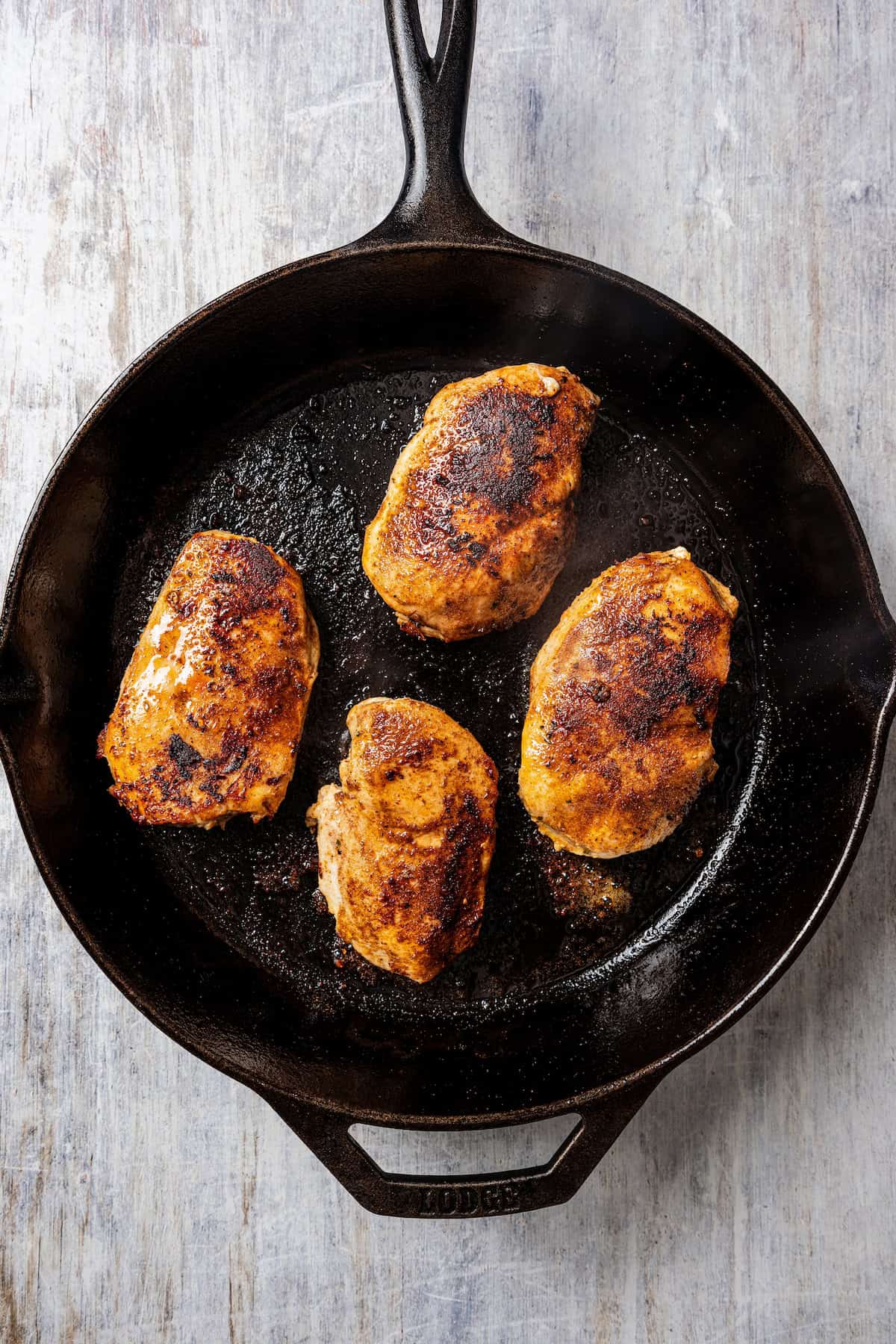 Four Jamaican jerk chicken breasts seared in a cast iron skillet.