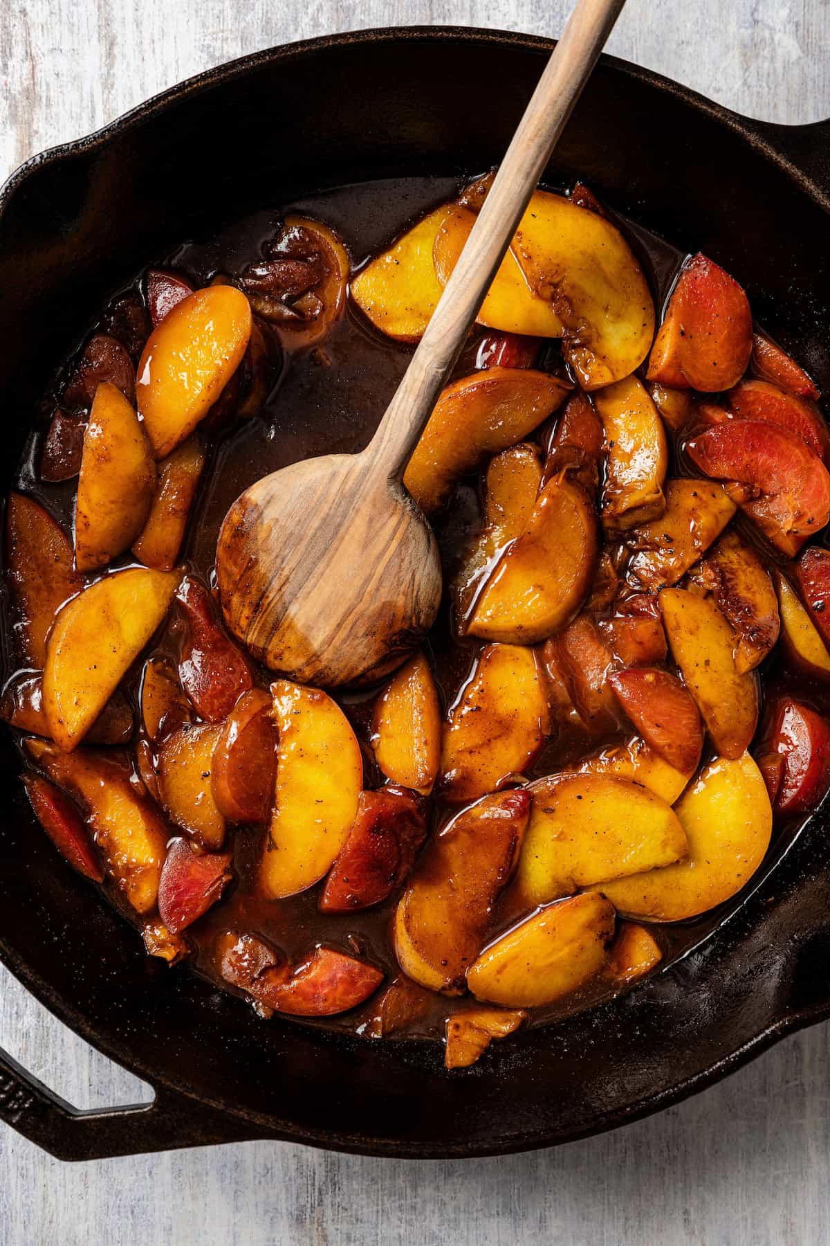 Sautéed peaches and plums in a cast iron skillet with a wooden spoon.