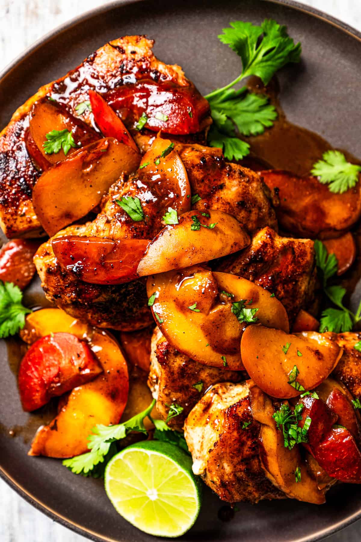 Close-up photo of cooked chicken breasts topped with peaches and plums sauce and garnished with half a lime.