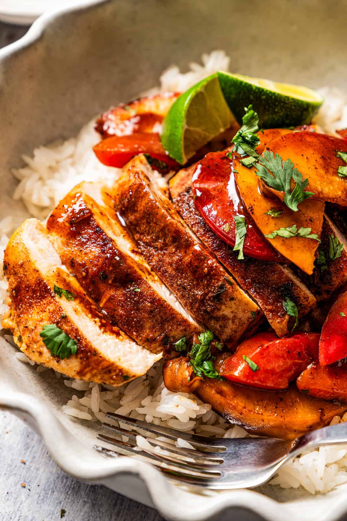 Up close image of sliced chicken breast topped with peaches, plums, and lime, and served over white rice.