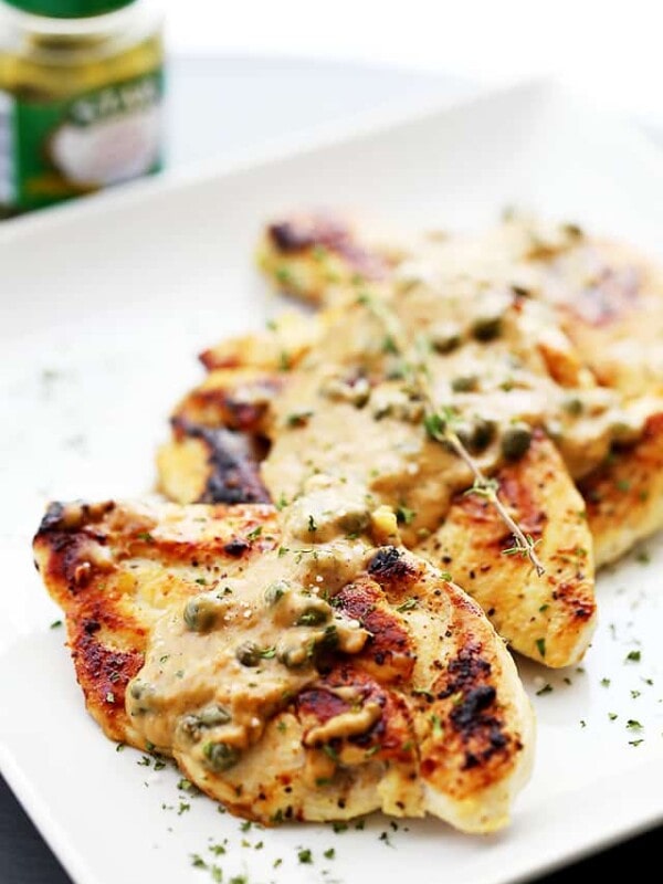 Chicken in a creamy lemon and caper sauce next to a jar of capers