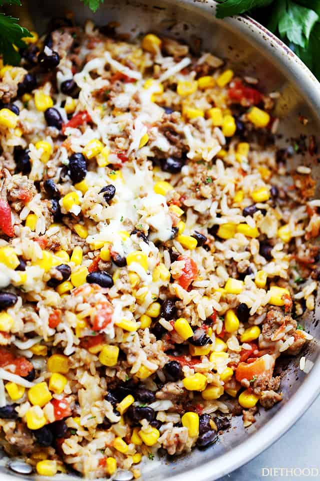 cooking ground beef, rice, corn kernels, black beans, and tomatoes in a stainless steel skillet.
