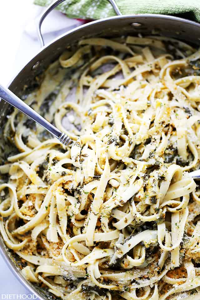 Overhead close up view of spinach fettuccine in a skillet with a serving spoon.