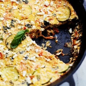 Zucchini frittata in a cast iron skillet with a slice missing.