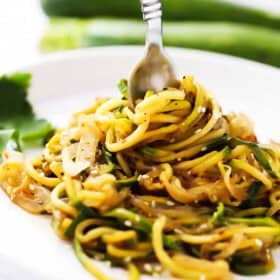 A fork stuck into a pile of stir fry zucchini noodles on a plate.