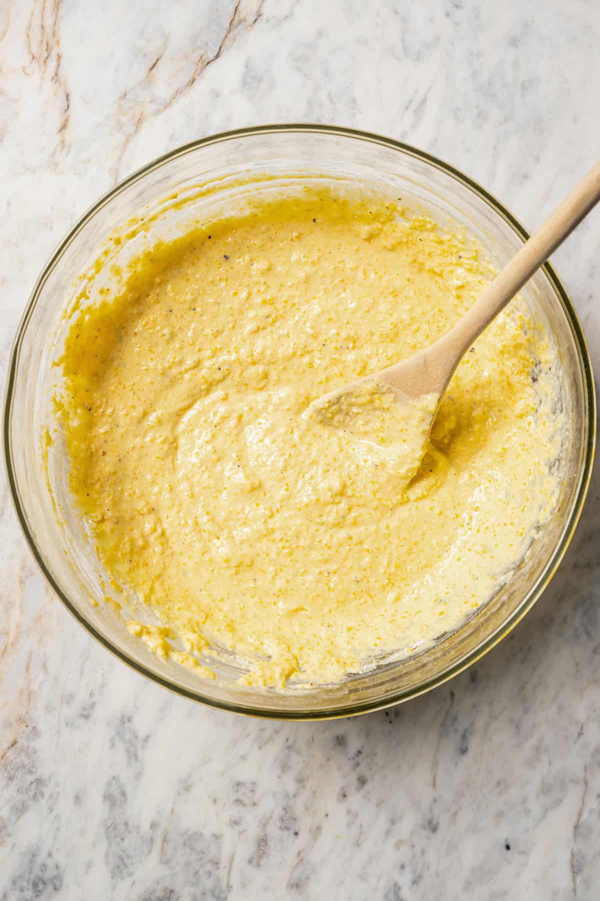 Cornbread pancake batter in a glass bowl with a wooden spoon.