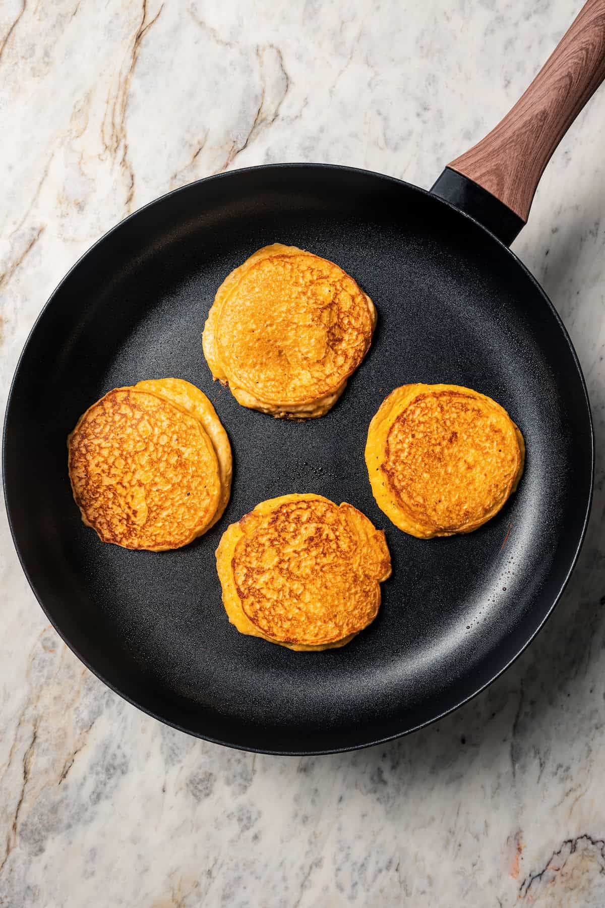 Four cornbread pancakes cooking in a cast iron skillet.