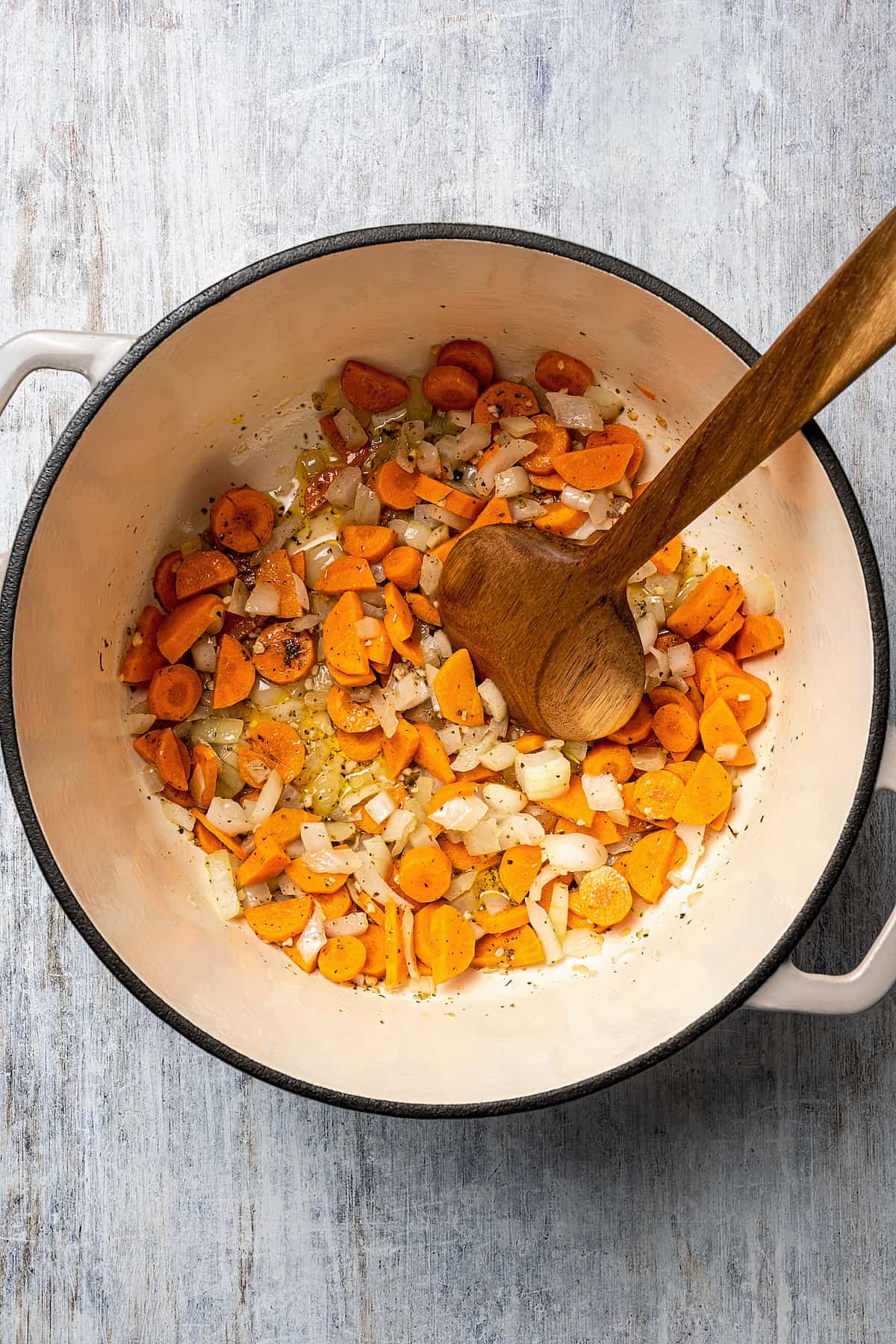 Sautéed onion, garlic, and carrots in a pot with a stirring spoon.