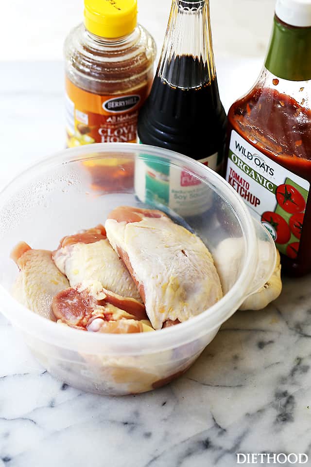 Honey, soy sauce, ketchup, raw chicken thighs, and garlic on a marble countertop.