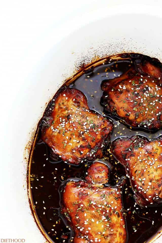 Cooked honey garlic chicken, garnished with sesame seeds, in a crockpot insert.