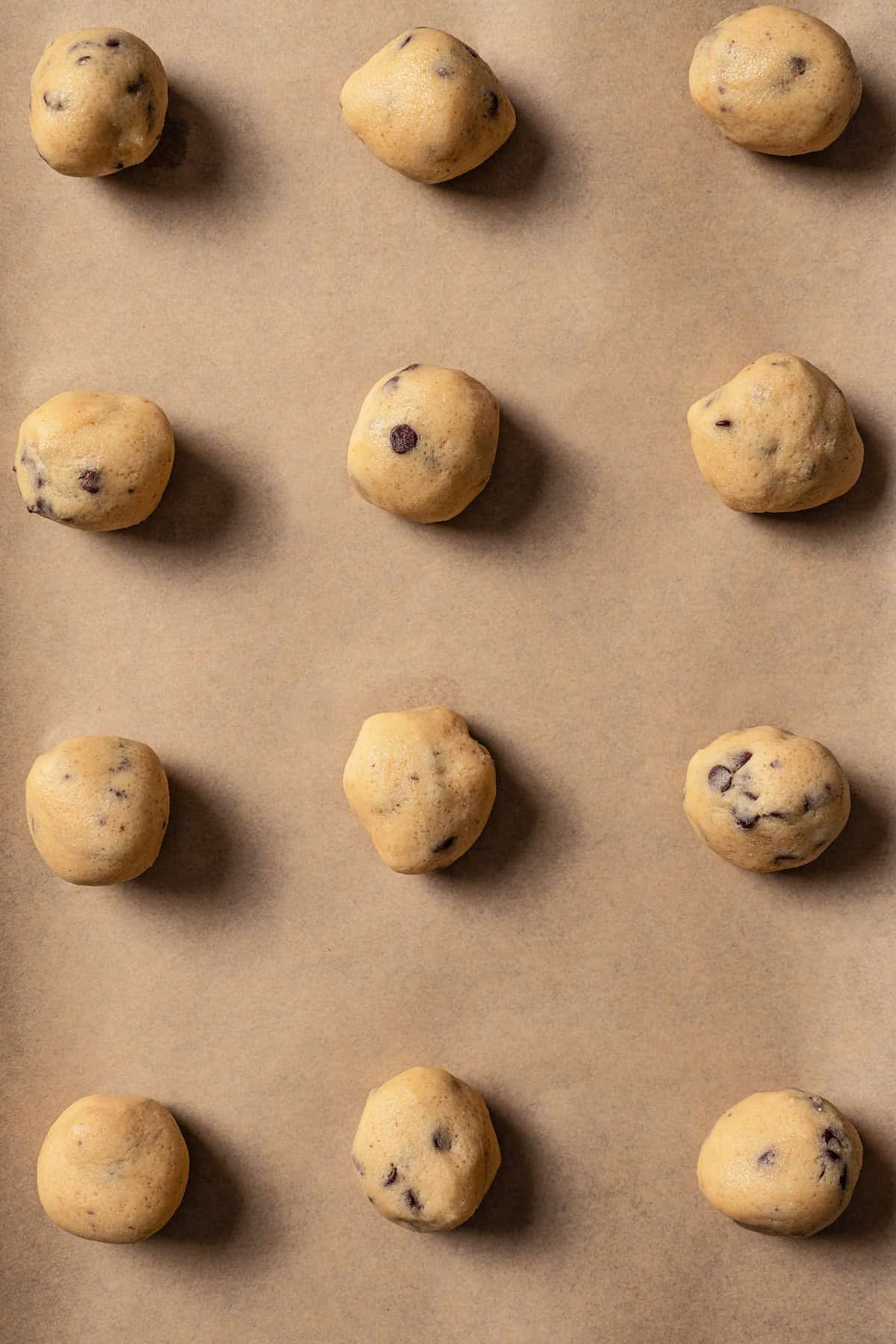 Rows of cookie dough balls on a parchment-lined baking sheet.