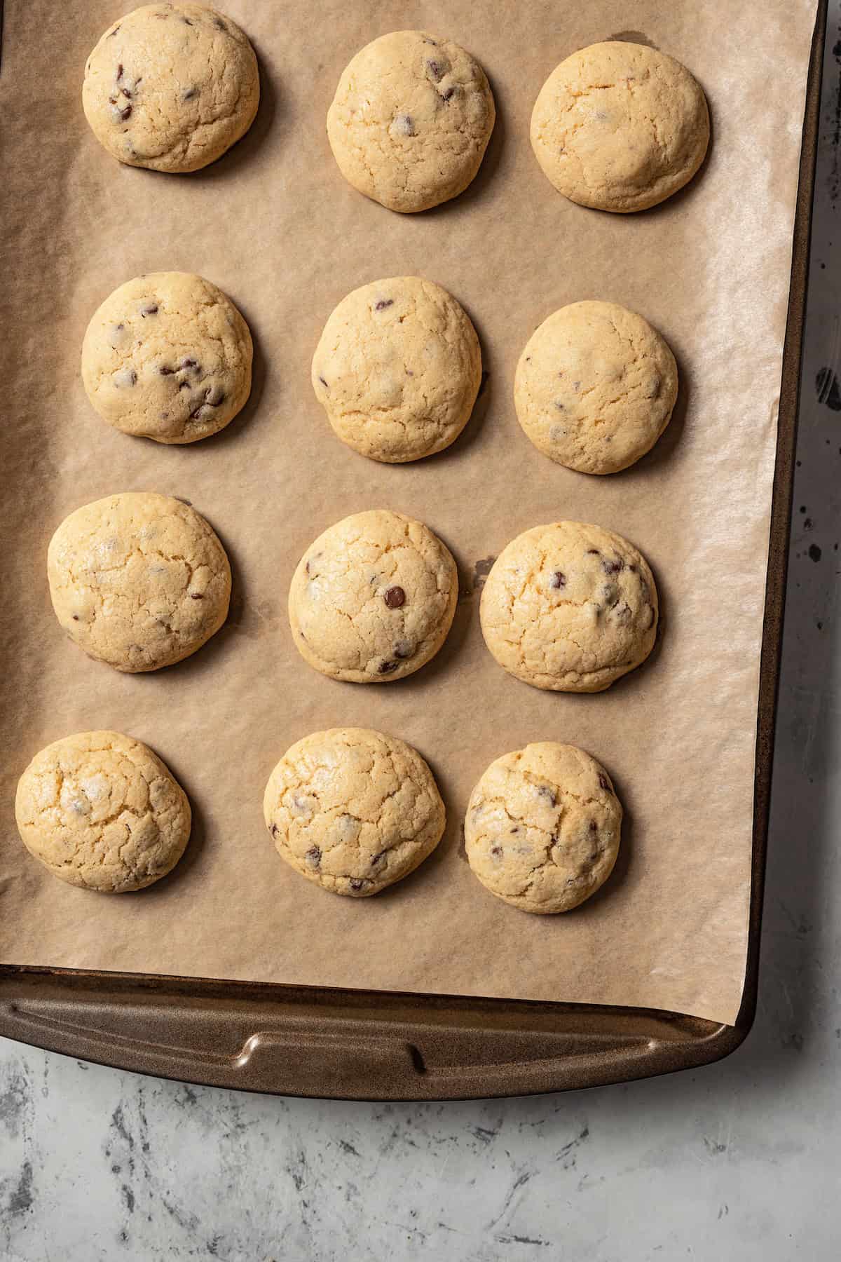 Rows of baked mini chocolate chip cookies on a lined baking sheet.