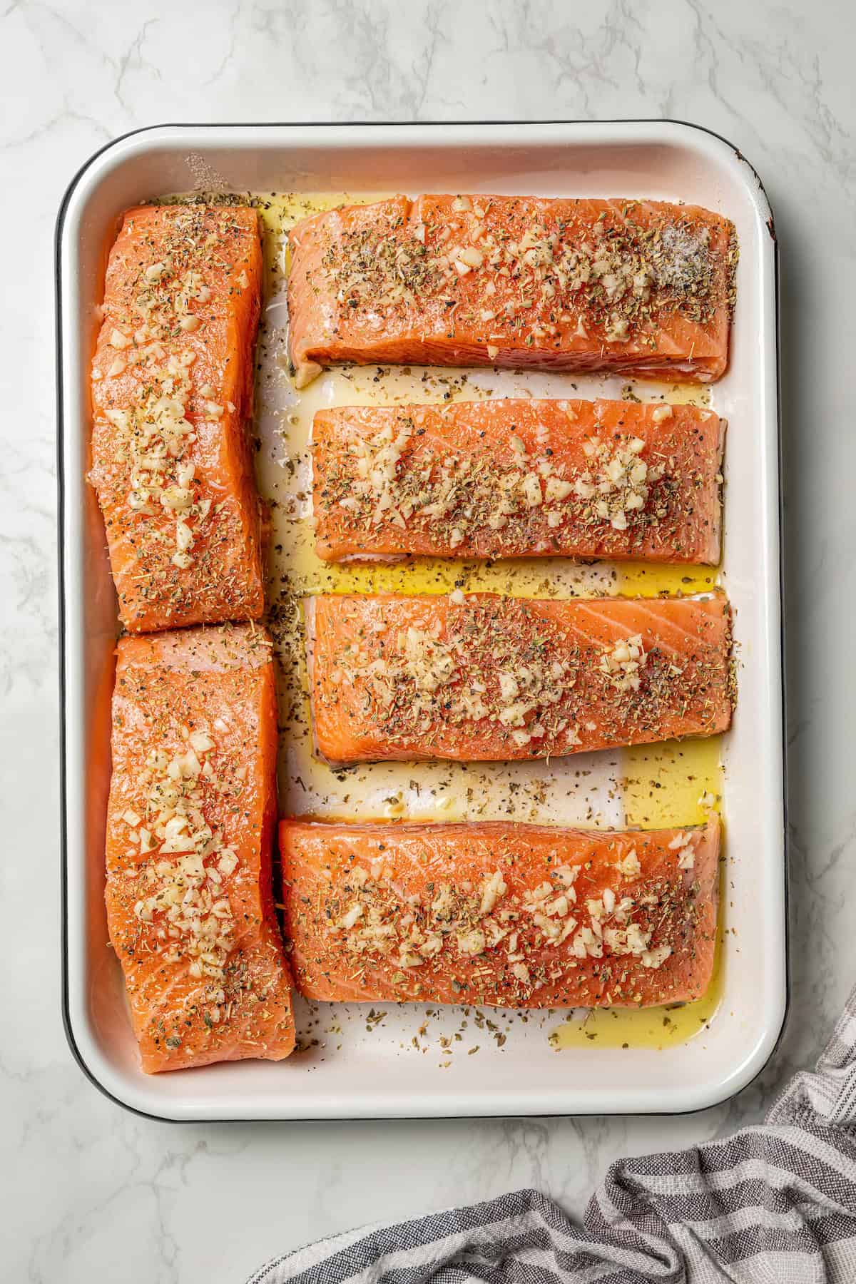 Overhead view of salmon fillets seasoned with minced garlic, salt, and pepper on a baking sheet.