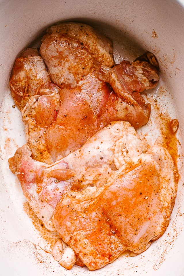 Boneless skinless chicken thighs are arranged inside the slow cooker.