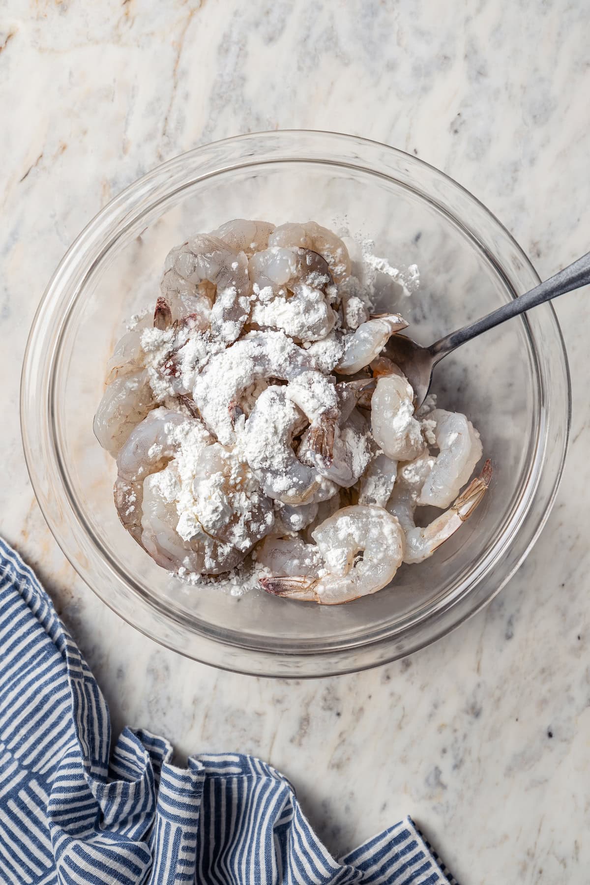 Cornstarch added to raw shrimp in a glass bowl.